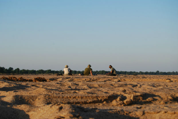 Three safari guide students sit on the banks of the Limpopo River waiting for the sun to go down.